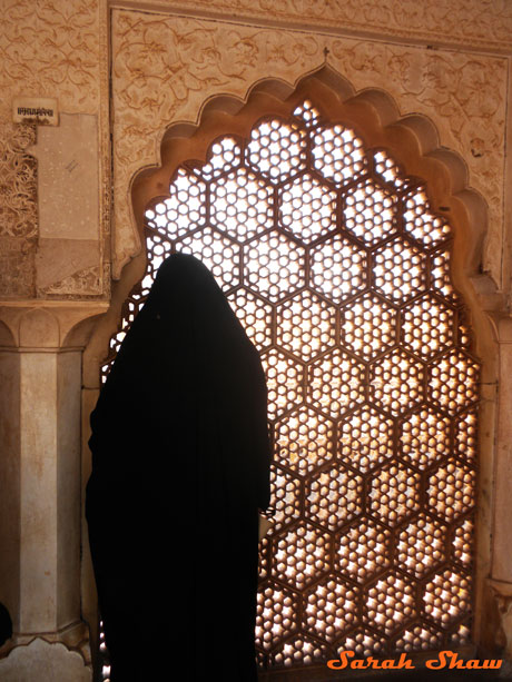 A woman gazes through a screen window at the Amber Fort in Jaipur, India
