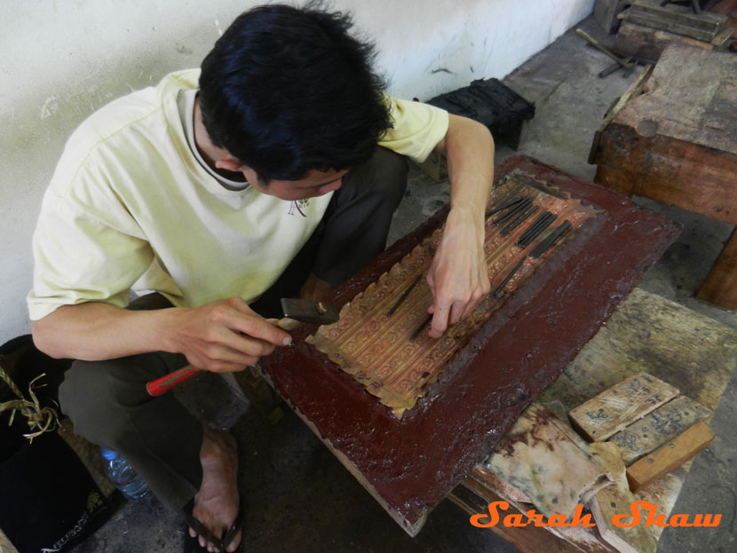 An apprentice molds silver to a form to create an embossed item at Artisans Angkor