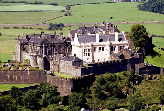 Stirling Castle atop a rocky hill surrounded by green landscape under a bright blue sky in Scotland